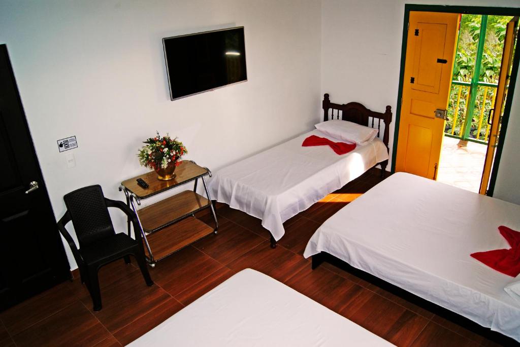 a room with two beds and a table and a television at Hostal Casa de Los Taitas in Salento