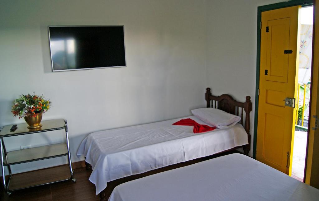 a bedroom with two beds and a tv on the wall at Hostal Casa de Los Taitas in Salento