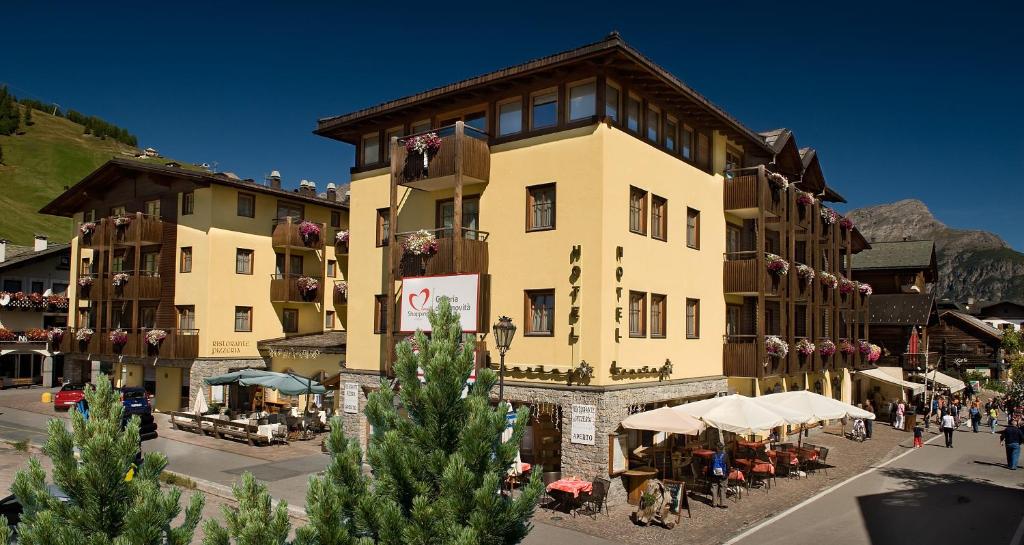 Un grand bâtiment jaune avec des personnes assises à l'extérieur dans l'établissement Hotel Touring, à Livigno