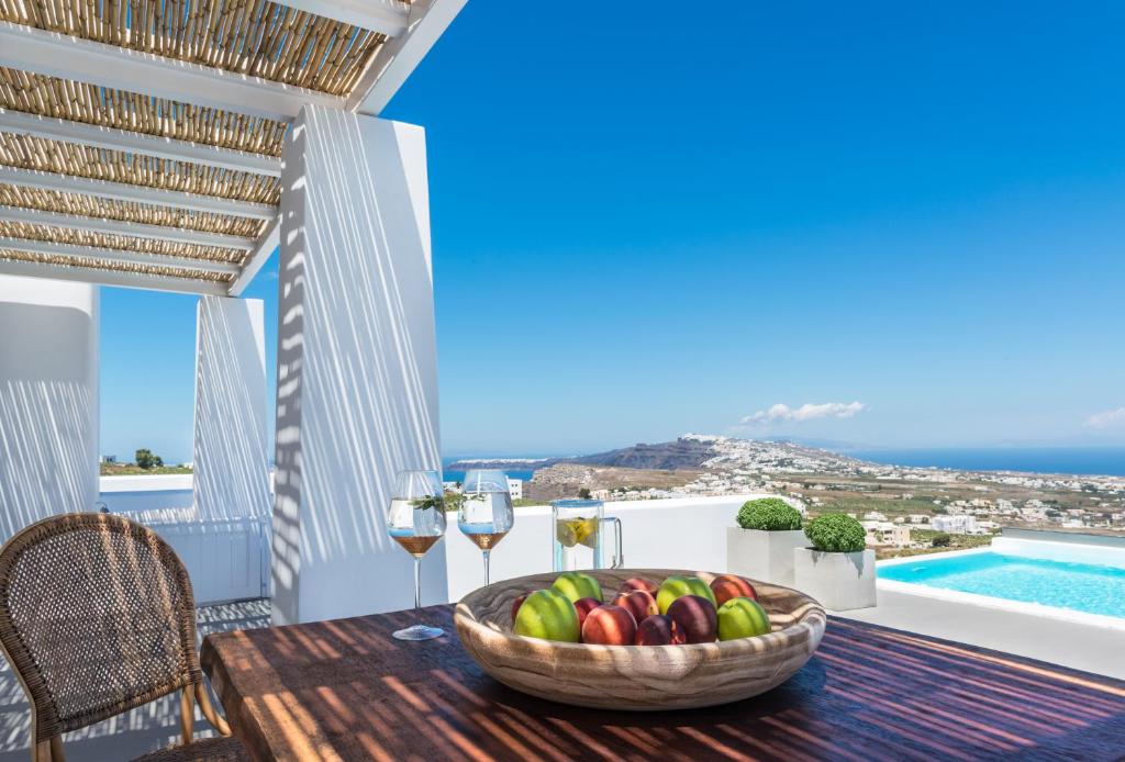 una mesa con un bol de frutas y copas de vino en el balcón en White & Co. Exclusive Island Villas, en Pirgos