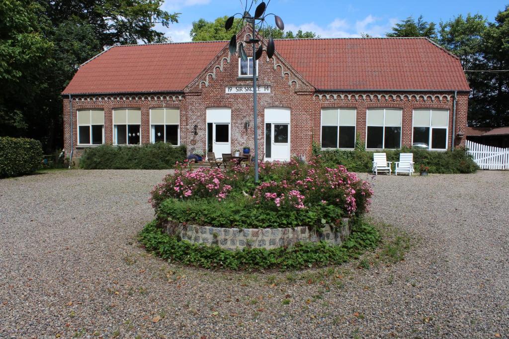 a brick building with a red roof with flowers in front of it at Sir Gamle Skole Holstebro in Holstebro