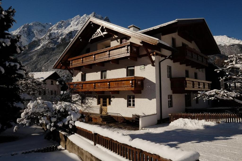 a building with snow on the ground next to a mountain at Gästehaus Schöpf Elsa in Längenfeld