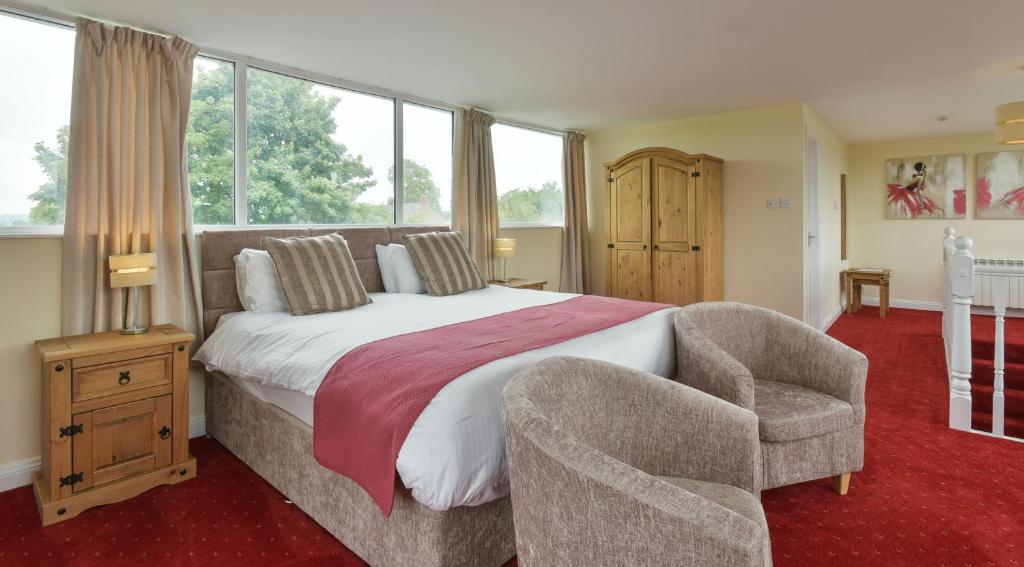 a bedroom with a bed and a chair and windows at Edenhall Country Hotel in Penrith