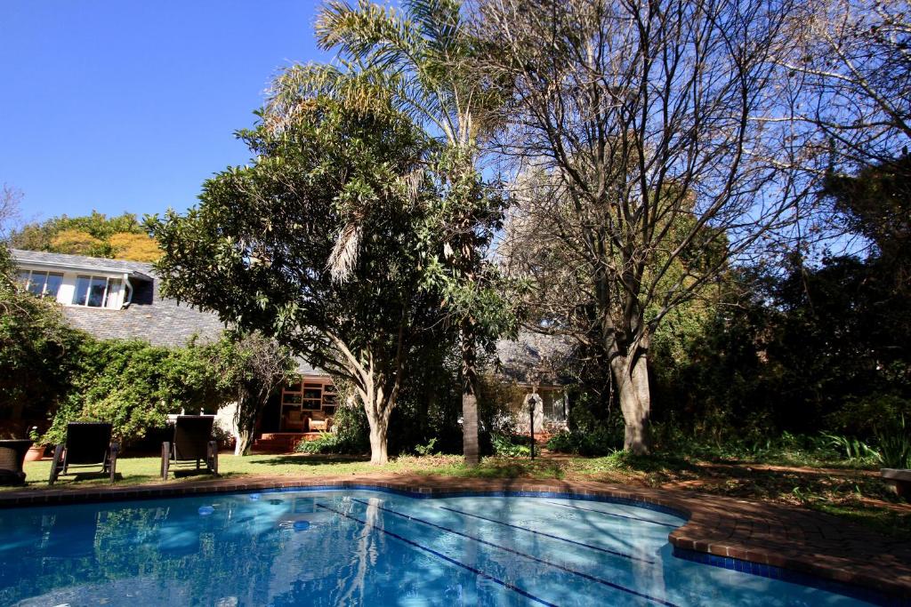 a swimming pool in front of a house with trees at Melrose Place Guest Lodge in Johannesburg