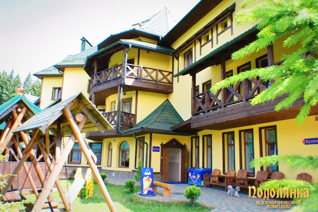 une grande maison jaune avec une aire de jeux devant elle dans l'établissement Podolyanka, à Slavsko