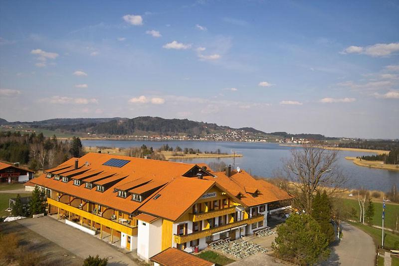 a large building with an orange roof next to a lake at Landhotel Wiesbauer in Füssen