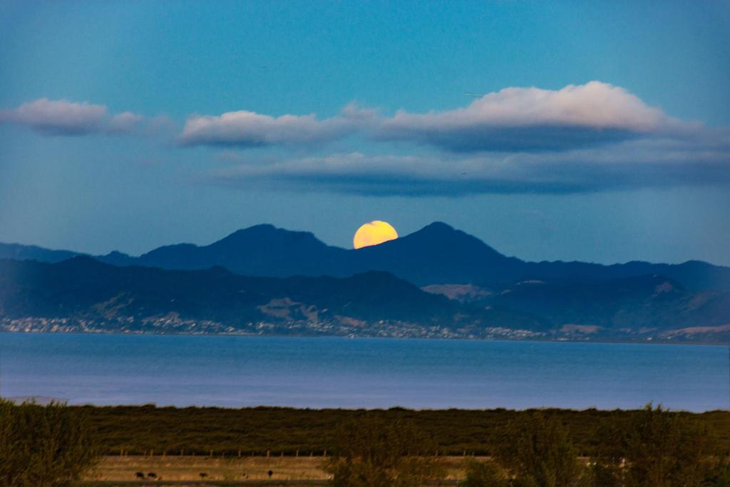una luna llena elevándose sobre las montañas y el agua en Miranda Sea View Apartment en Miranda