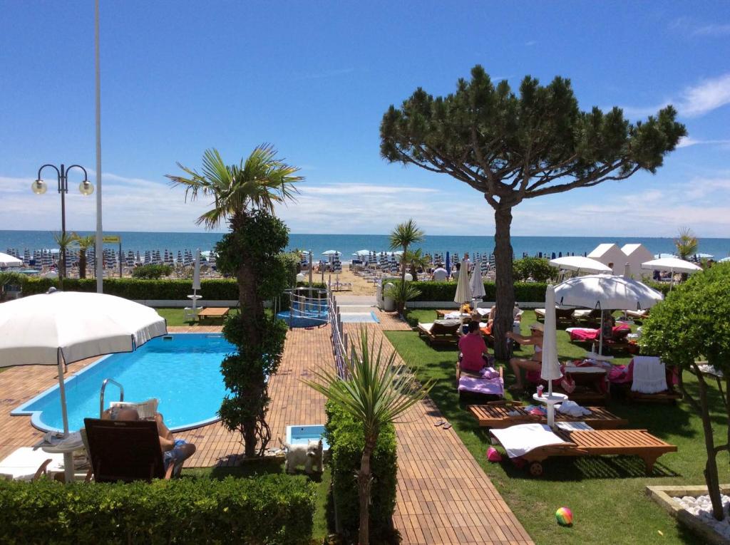 a resort with a swimming pool and people sitting in chairs at Hotel Universo in Lido di Jesolo