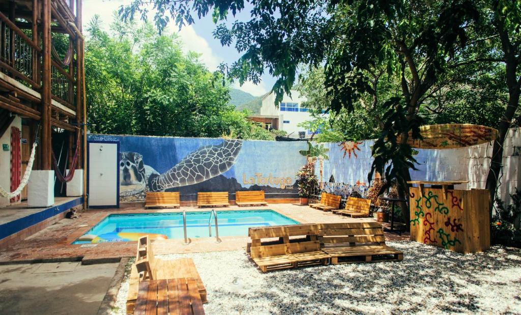 a pool with chairs and a fence with a mural at La Tortuga Hostel in Taganga