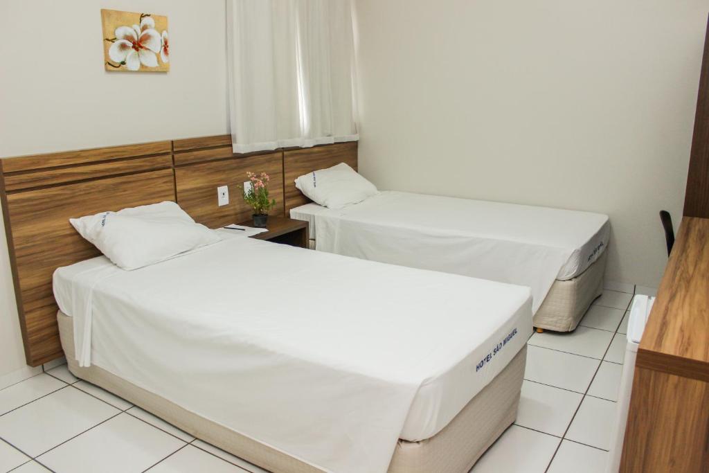 two beds in a hotel room with white sheets at Hotel São Miguel in Sorriso