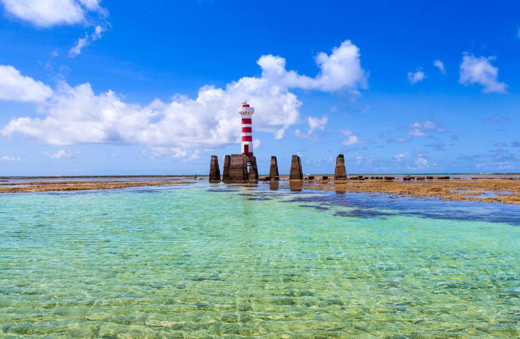 a red and white lighthouse in the water next to a beach at Sun Paradise - Pio X in Maceió