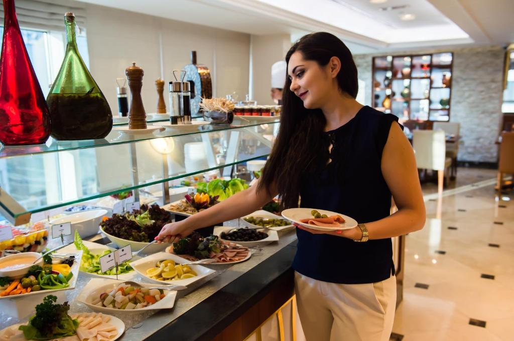 a woman holding a plate of food at a buffet at Grand Mercure Majlis Residences in Abu Dhabi