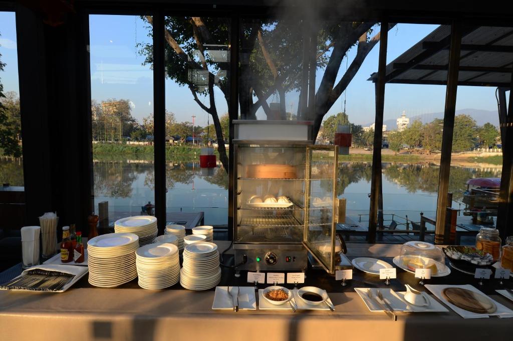 A breakfast buffet beside floor-to-ceiling windows overlooking water and trees.
