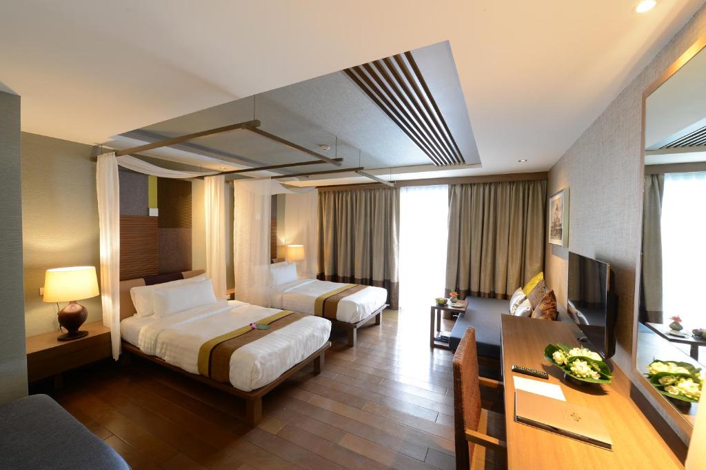 A twin room with a desk, television, sofa edge, and curtained window wall.