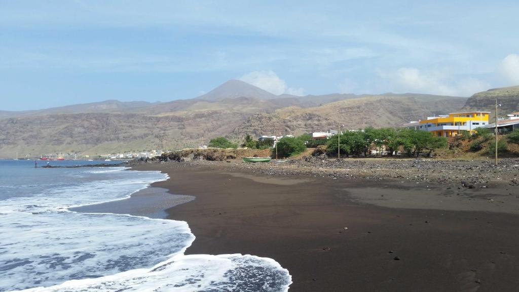 ein schwarzer Strand mit Häusern und Bergen im Hintergrund in der Unterkunft Casa Patio in Tarrafal