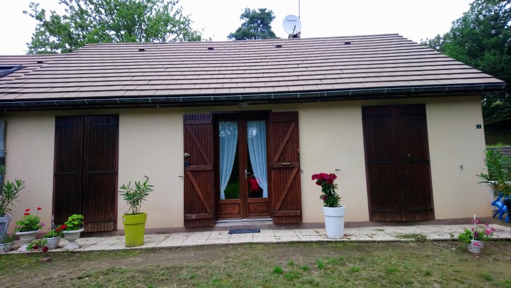 une petite maison avec des portes en bois et des fleurs dans une cour dans l'établissement Maison Bord Du Lac, à Marcillac-la-Croisille