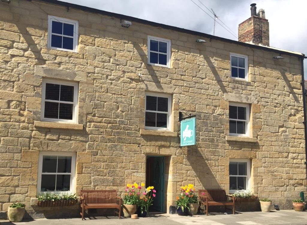 a stone building with benches and flowers in front of it at Bertram's in Warkworth