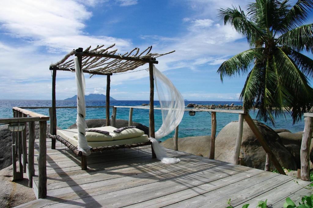 a bed on a wooden deck next to the ocean at Bliss Boutique Hotel Seychelles in Glacis