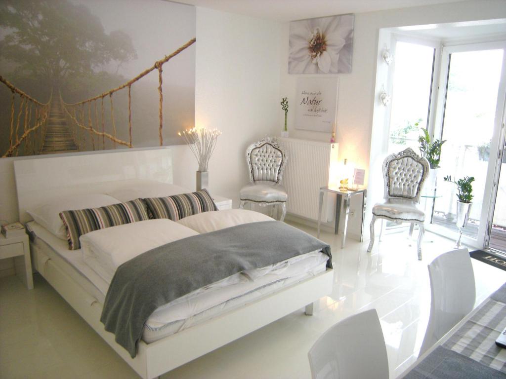a white bedroom with a bed and two chairs at A-Partments in Cologne