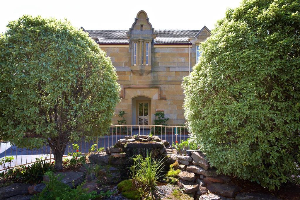an old building with trees in front of a garden at Quest Trinity House in Hobart
