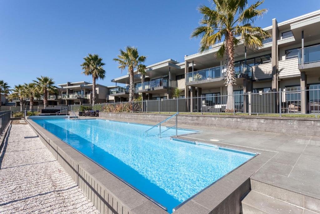 a swimming pool in front of a building with palm trees at Sovereign Pier On The Waterways in Whitianga