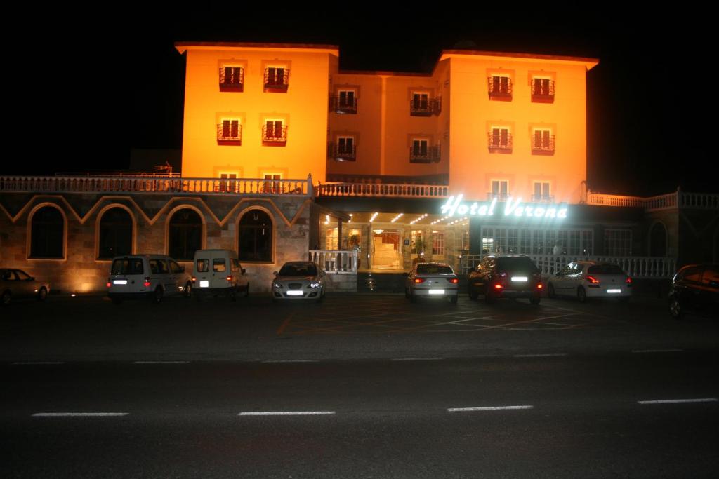 een gebouw met auto's geparkeerd op een parkeerplaats 's nachts bij Hotel Verona in Puertollano