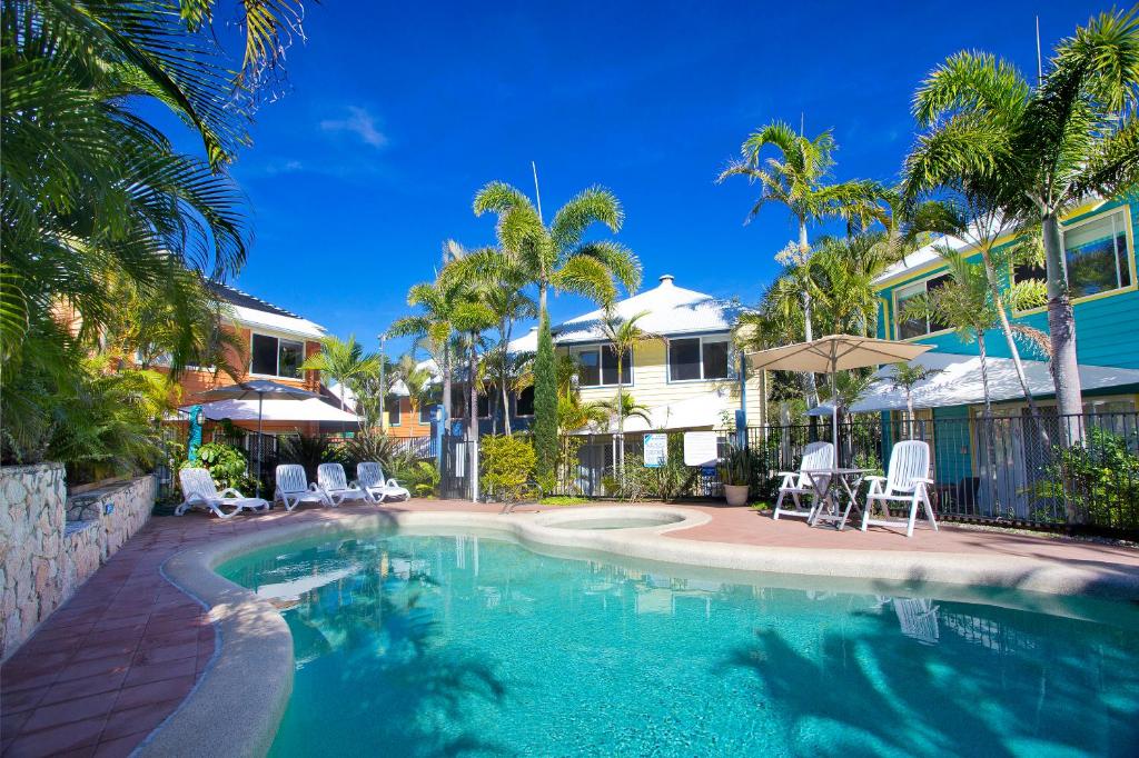 a swimming pool with chairs and umbrellas next to a house at Sails Lifestyle Resort in Peregian Beach