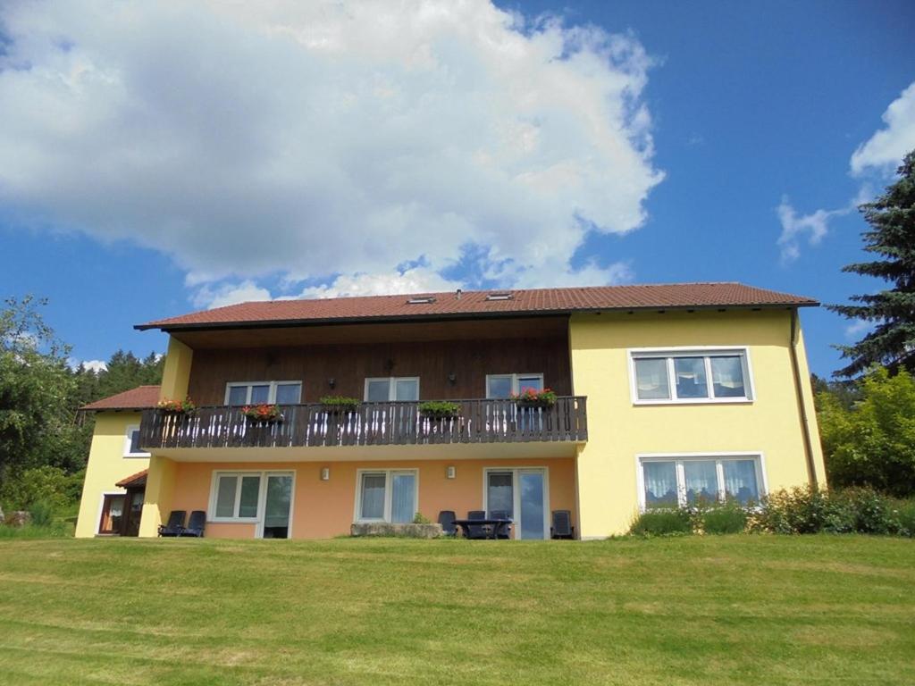 a yellow house with a balcony on a lawn at Ferienhaus Bauer mit wunderschönem Panoramablick in Tännesberg