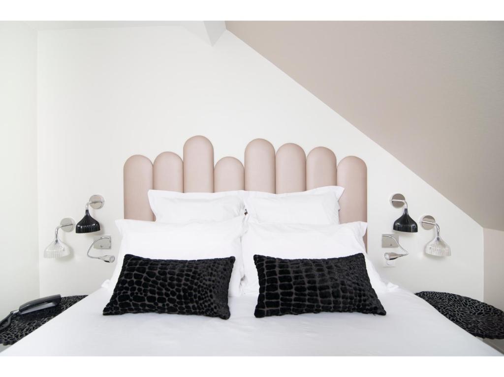 a bedroom with a white bed with black and white pillows at Hotel Restaurant Les Capucins in Belfort