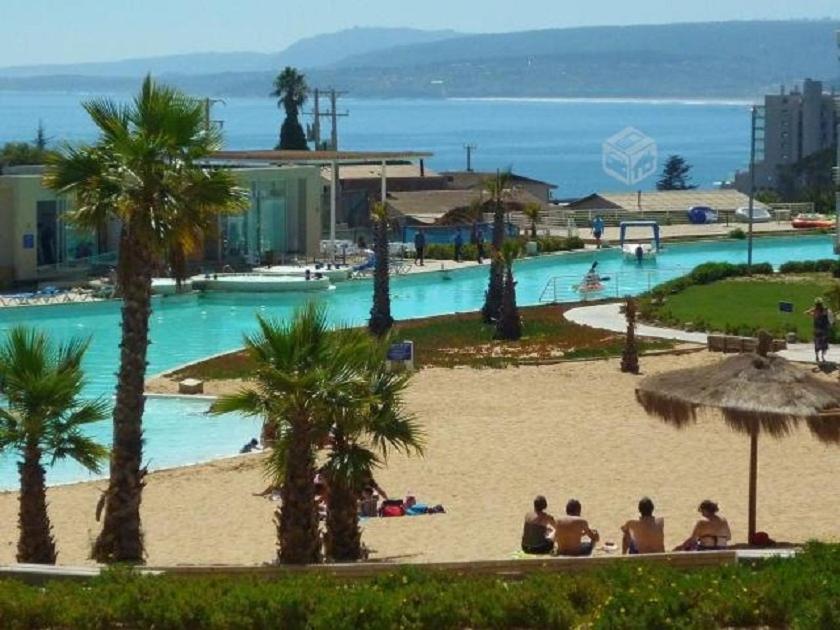 un grupo de personas sentadas en la playa cerca de una piscina en Departamento Laguna Vista Algarrobo, en Algarrobo