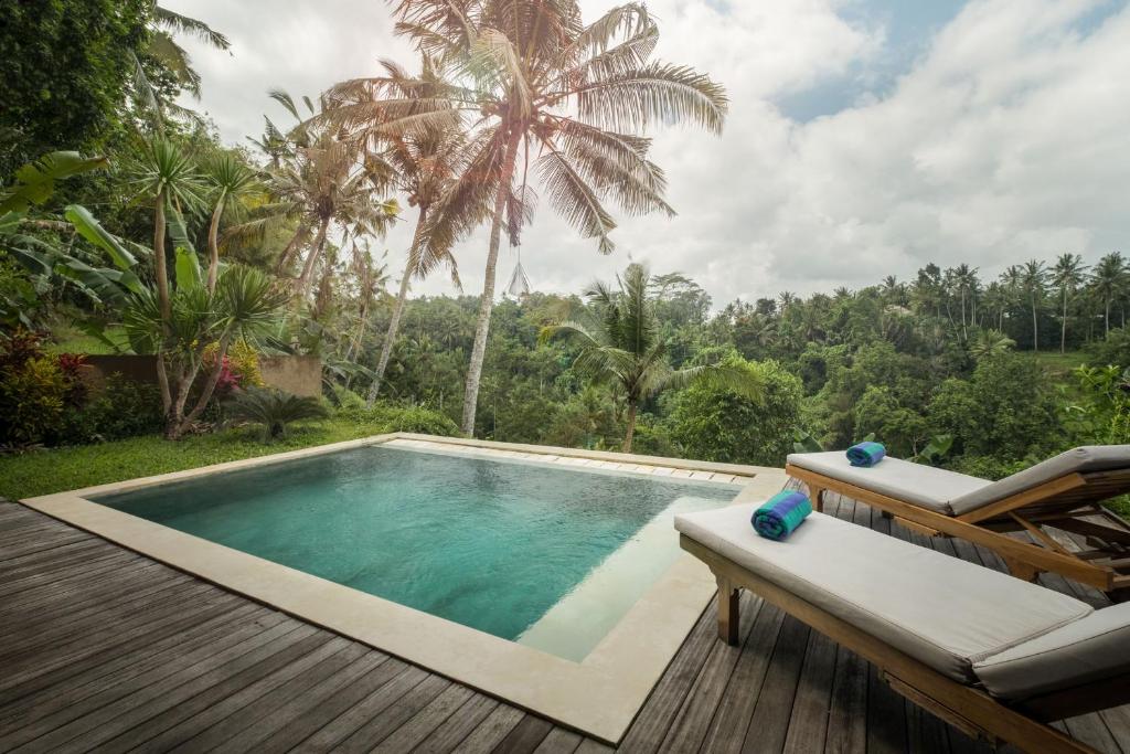 a pool with a deck and chairs and a palm tree at Villa Tepi in Ubud