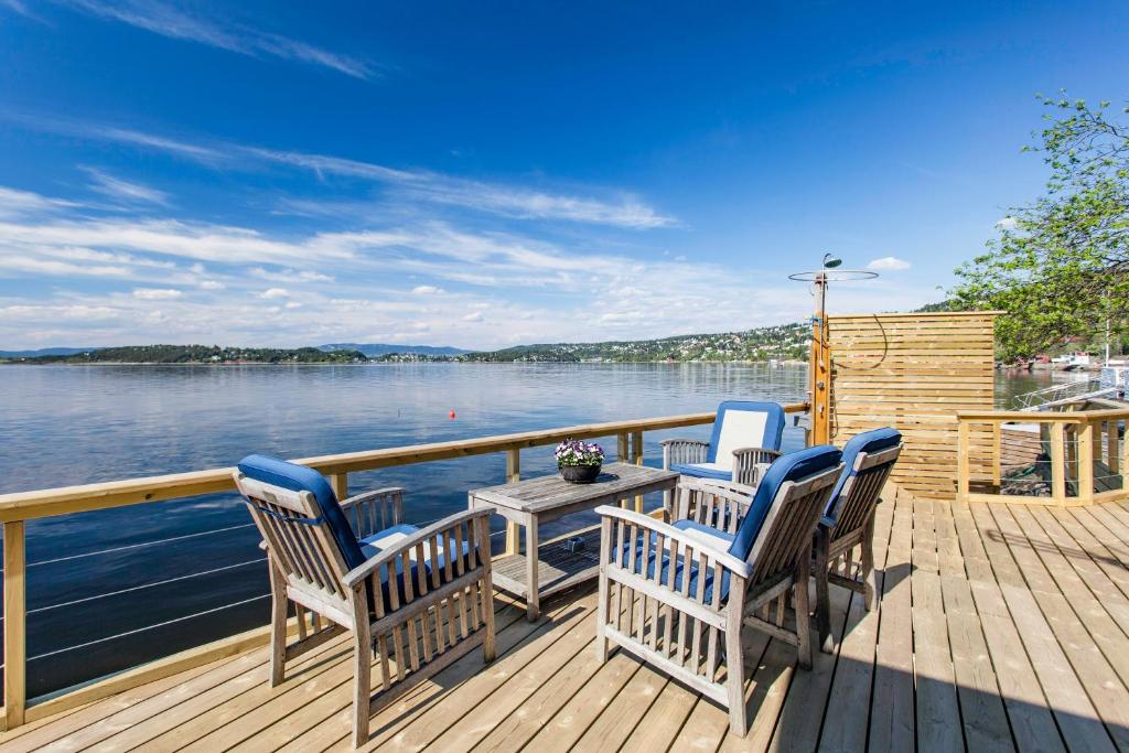 Beach house in Oslo في أوسلو: سطح السفينة به ثلاثة كراسي وطاولة على الماء