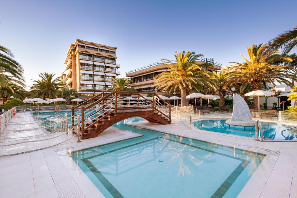 una piscina en un complejo con un puente y palmeras en Hotel Caesar Residence & SPA en Lido di Camaiore