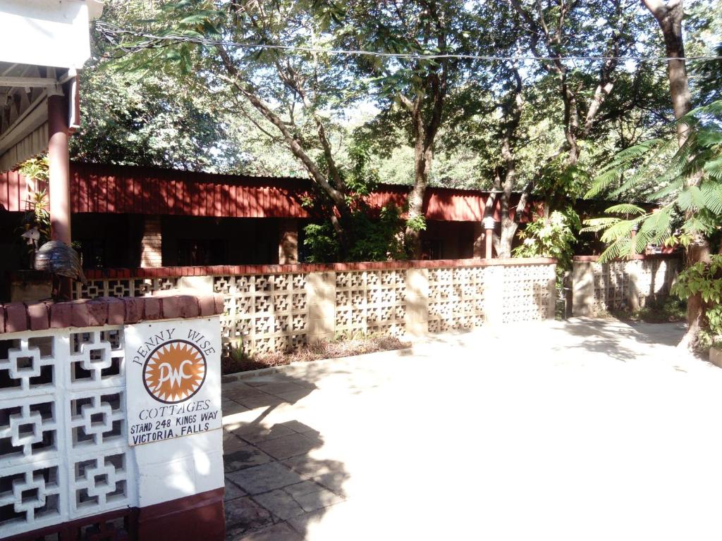 a white fence with a sign in front of a building at Pennywise Cottages in Victoria Falls