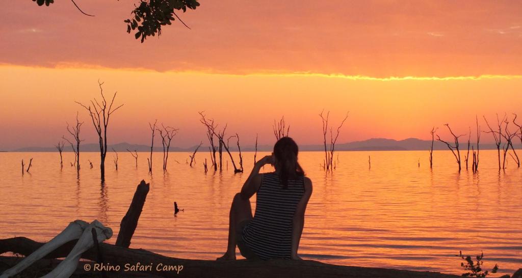 a woman sitting on the shore of a lake at sunset at Rhino Safari Camp in Bumi Hills