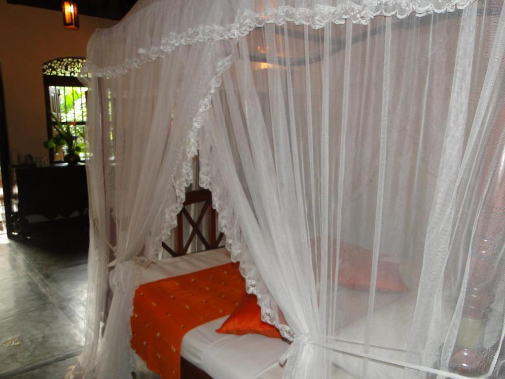 a canopy bed with white curtains in a room at Thambapanni Retreat in Unawatuna