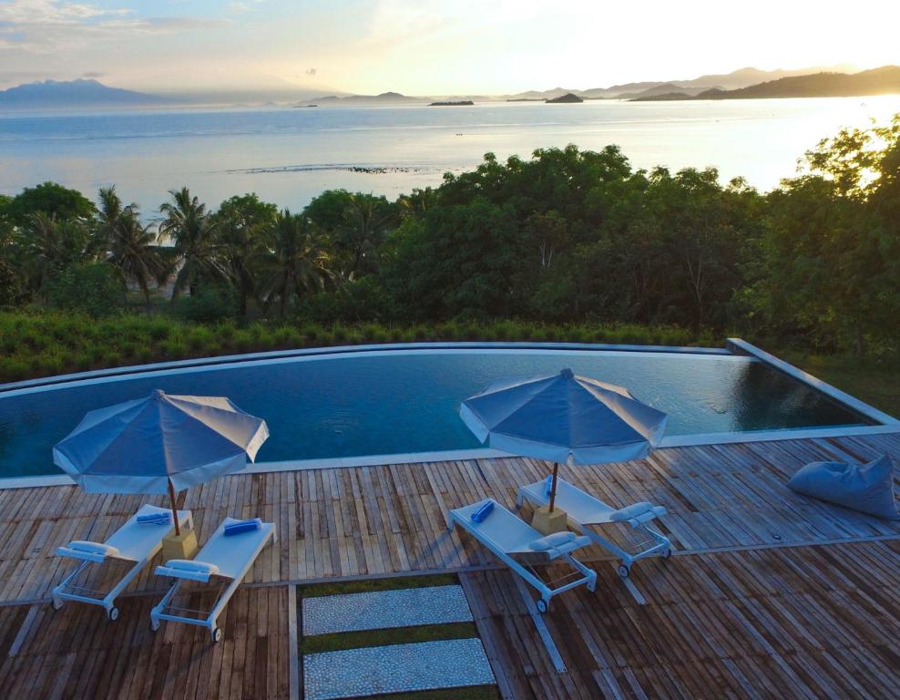 a pool with chairs and umbrellas on a deck at Villa Selalu in Gili Gede