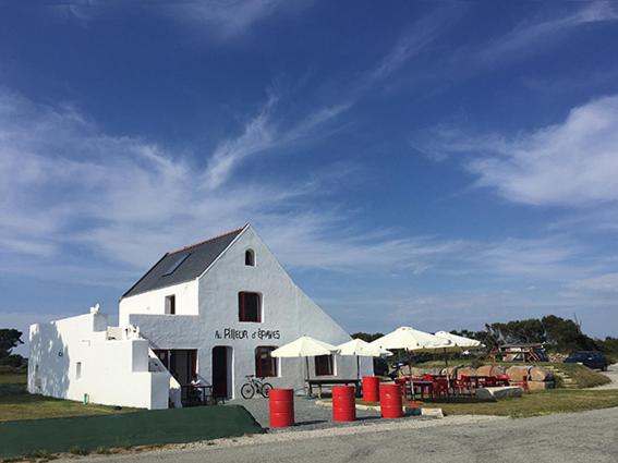 Un bâtiment blanc avec des tonneaux rouges devant lui dans l'établissement Le Pilleur d'Epaves, à Cléden-Cap-Sizun