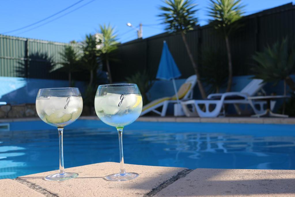 dois copos de vinho sentados numa mesa perto de uma piscina em Casa Teresinha em Sesimbra