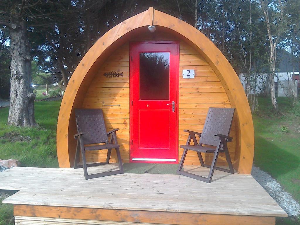 a red door and two chairs in a wooden cabin at Dunvegan Camping Pods in Dunvegan