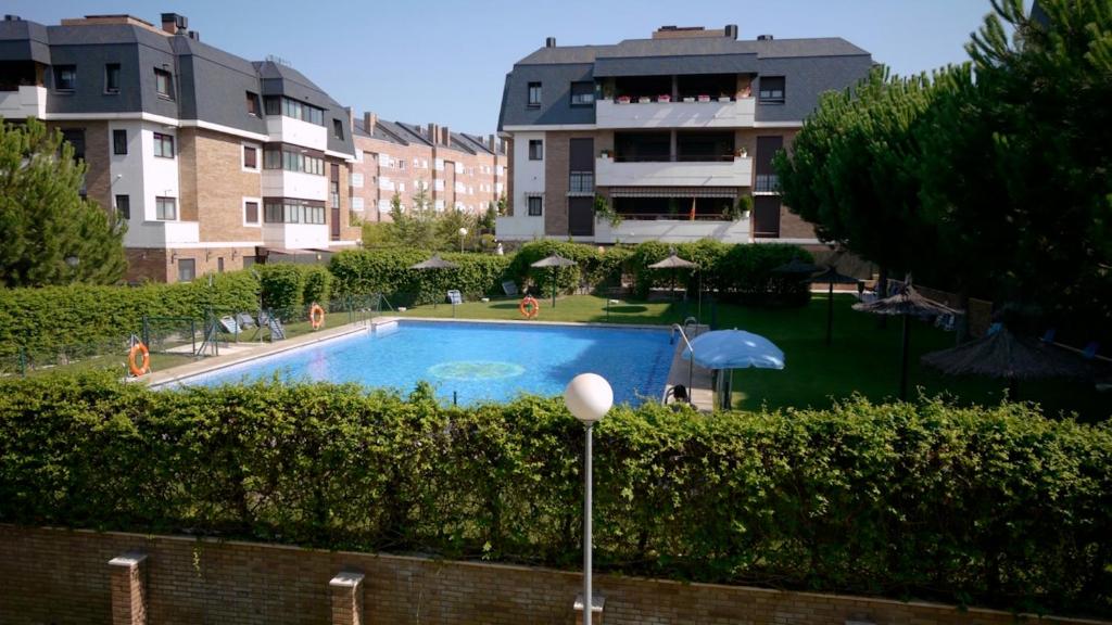 a swimming pool with an umbrella and some buildings at Golf Apartment in Majadahonda