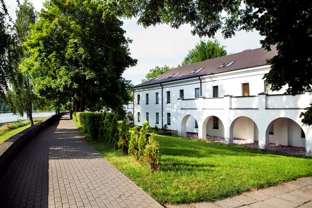 a white building with a sidewalk next to a grass field at Domus Hotel in Birštonas
