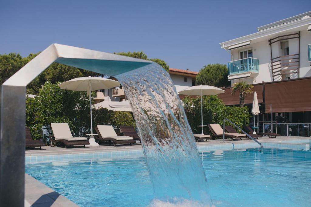 a fountain in a swimming pool with chairs and umbrellas at Park Hotel Ermitage Resort & Spa in Lido di Jesolo