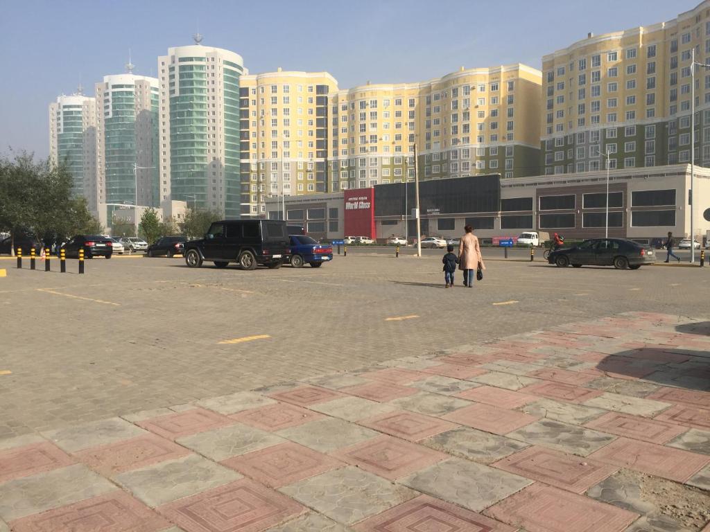 a woman and child walking in a parking lot with tall buildings at Квартира в 11 микрорайоне, жк. Арай in Aktobe