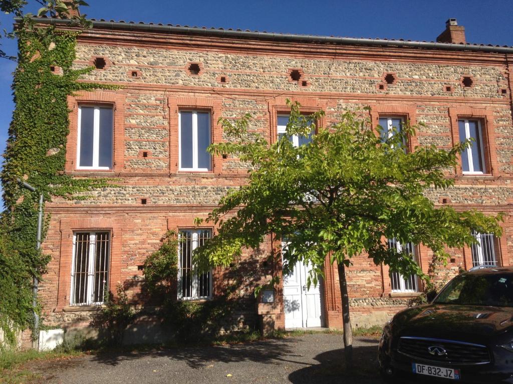 ein altes Backsteingebäude mit einem Baum davor in der Unterkunft Gentil'Home - Toulouse B&B Prestige in Fenouillet