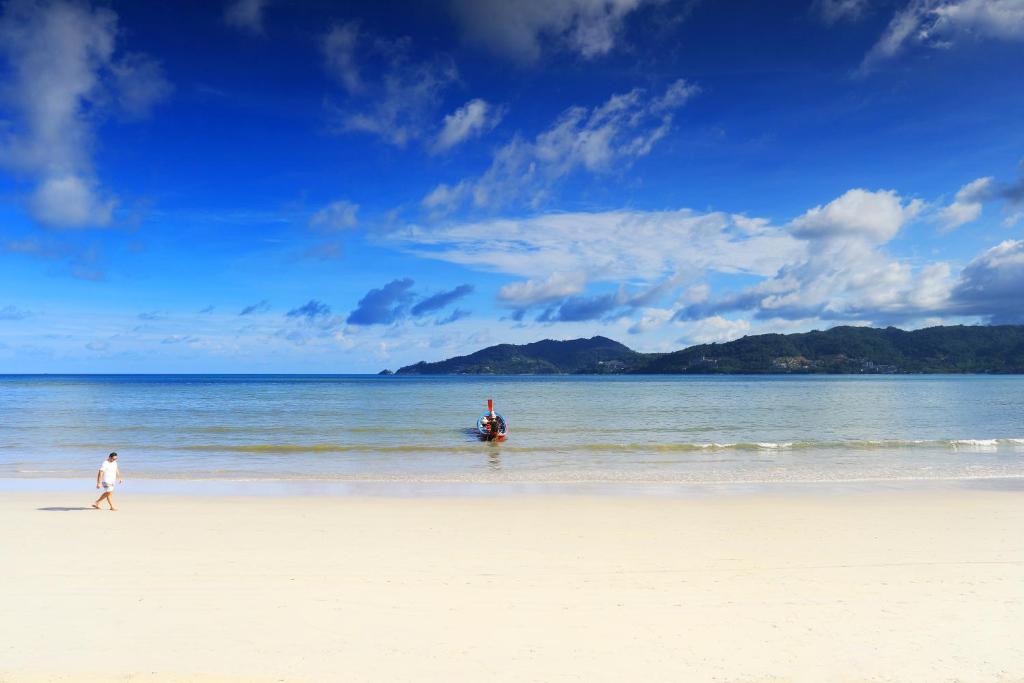 a person walking on a beach with a boat in the water at Baan Boa Resort in Patong Beach