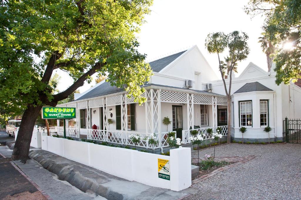 Uma casa branca com um cartaz à frente. em Oakdene Guest House em Oudtshoorn