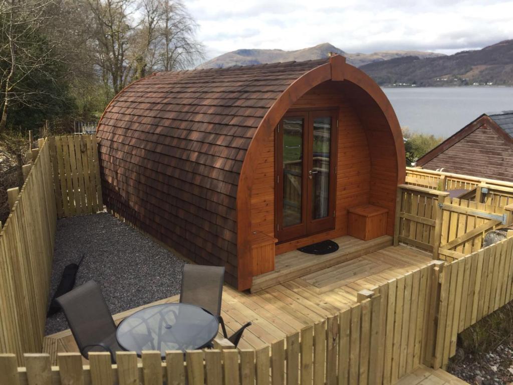 a large wooden cabin with a table and chairs on a deck at Seaview Pod and hot tub in Ballachulish