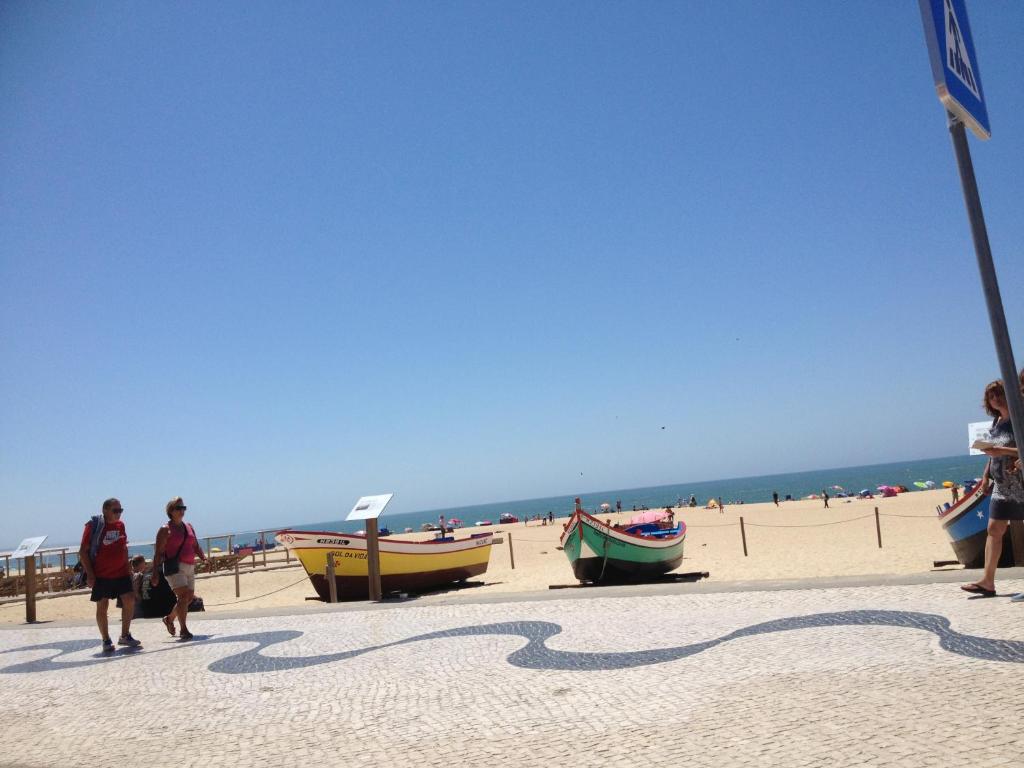 um grupo de pessoas caminhando em uma praia com barcos em Holidays Vista Mar Nazare na Nazaré