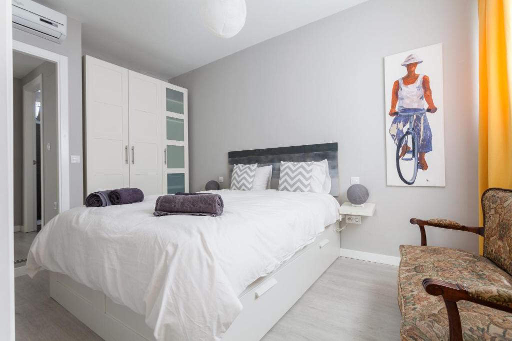 a white bedroom with a large bed and a chair at Suite Batihojas in Seville